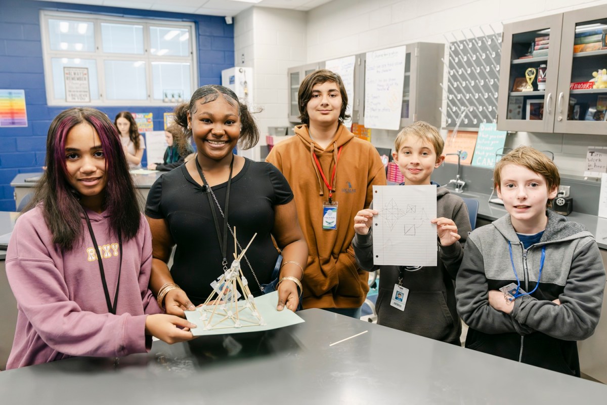A proud team of Highland Springs Middle School students showcase their complete structure alongside a design plan, highlighting their teamwork and creativity.